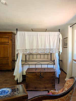 Camera Gigante di Fiandra, Poggio al Coniglio Suvereto: letto a baldacchino con tendaggi bianchi, cassapanca e luce naturale