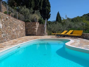 Piscina con solarium in pietra e lettini gialli tra cipressi — Poggio al Coniglio, villa in Toscana a Suvereto con camere in affitto