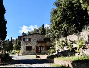 Ampia veranda coperta in pietra con tavolo da pranzo e vista sul giardino e le colline toscane.
