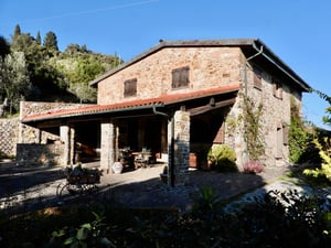 Facciata in pietra di una casa di campagna circondata da alberi e muretti in pietra.